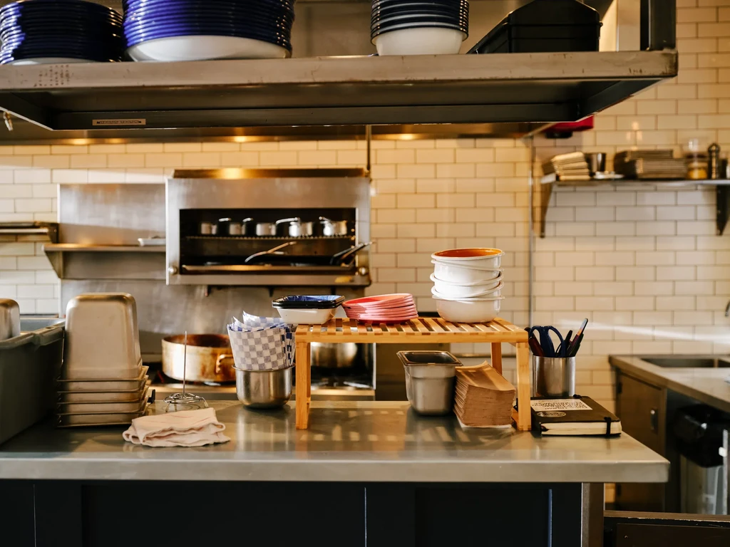 Clean professional kitchen with stainless steel counters, colorful plates, and cooking equipment.