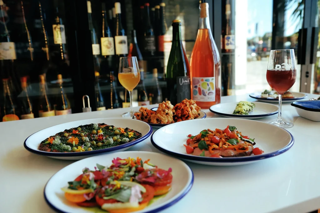 Multiple gourmet dishes, wine bottles, and glasses on a white table.