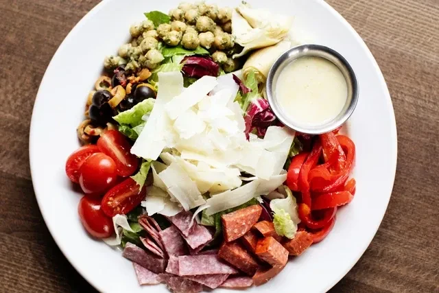 Overhead view of a vibrant salad with cheese, meats, vegetables, and dressing.