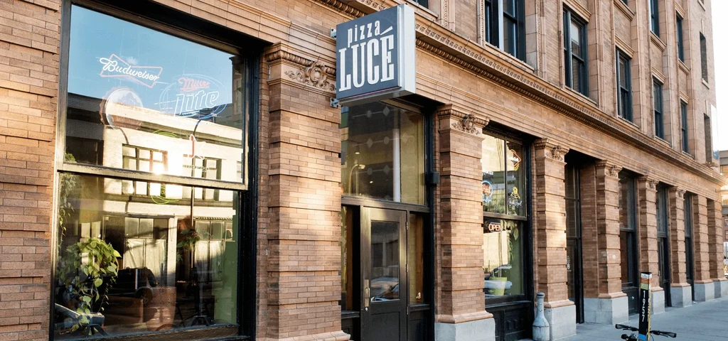 Ornate brick Pizza Luce restaurant, with neon bar signs visible.