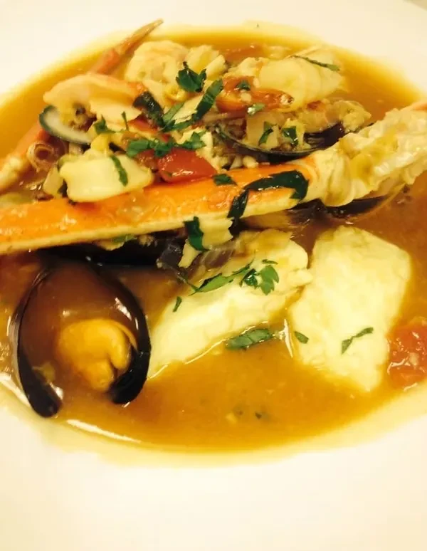 Close-up seafood stew with crab, mussels, fish, and herbs in broth.