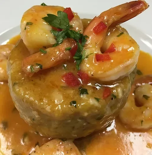 Close-up of mofongo with shrimp, creamy sauce, red peppers, and parsley.