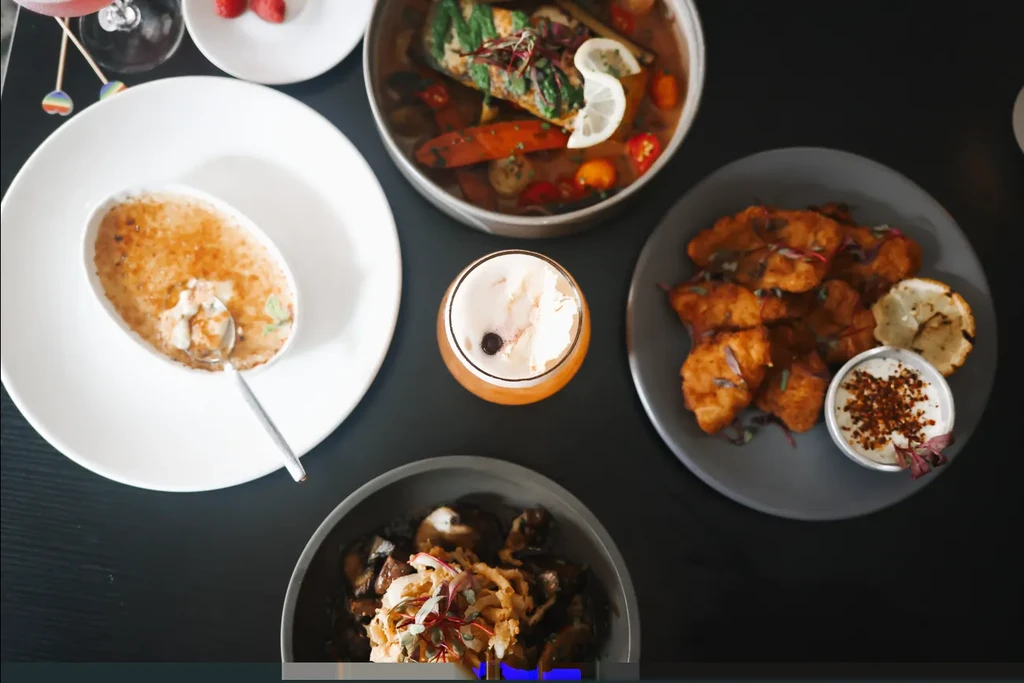 Overhead shot of a restaurant table with diverse dishes, dessert, and a drink.