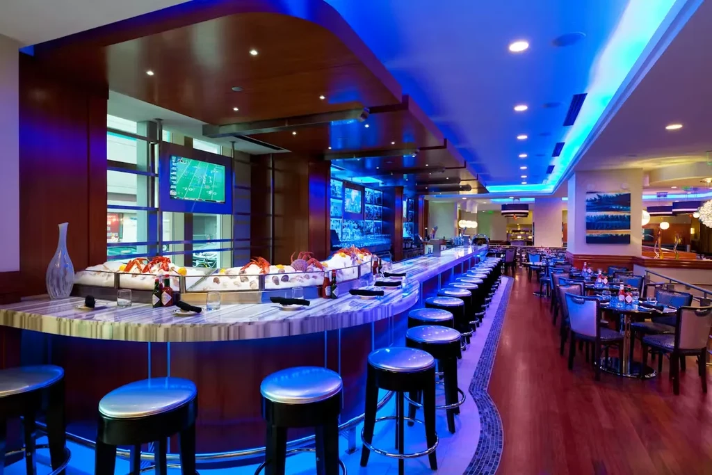 Modern restaurant interior featuring a raw bar and vibrant blue lighting.