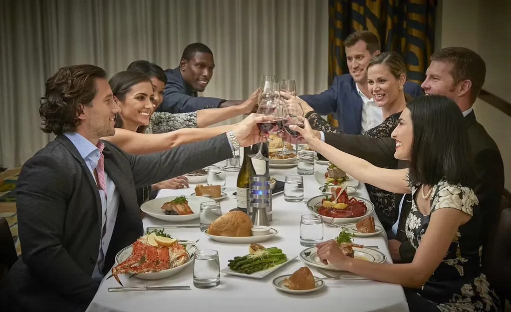 Eight people toast with red wine at an upscale restaurant table.