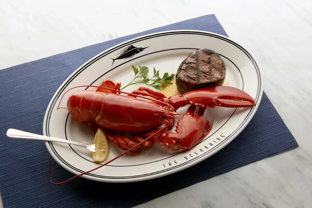 Cooked lobster and steak on 'THE OCEANAIRÉ' branded plate.