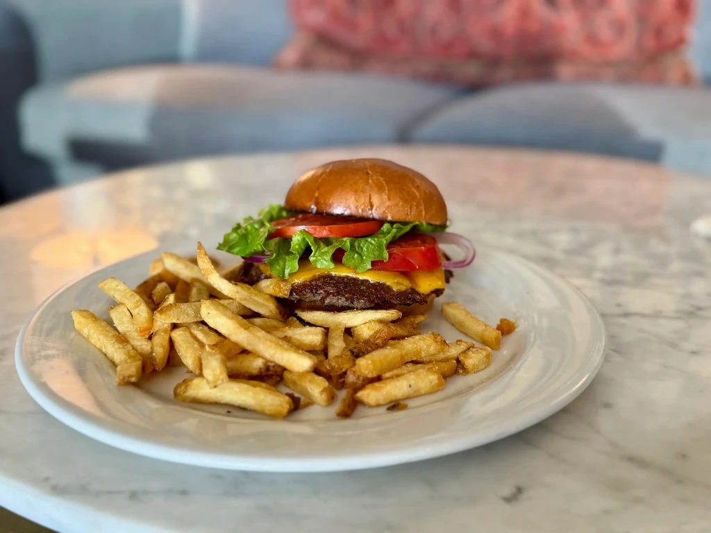 Plate with a double cheeseburger and golden french fries on a table.