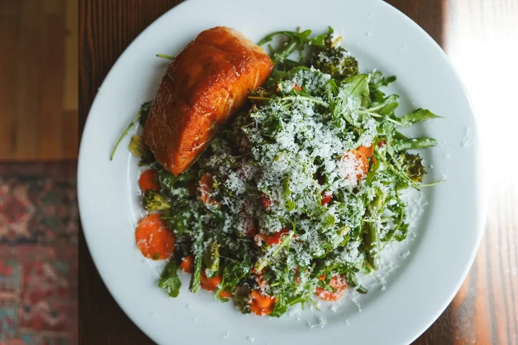 Glazed salmon on greens with carrots, broccoli, and grated cheese.