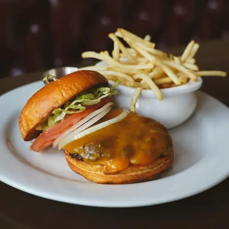 Open-faced burger with melted cheese, fresh vegetables, and golden french fries.