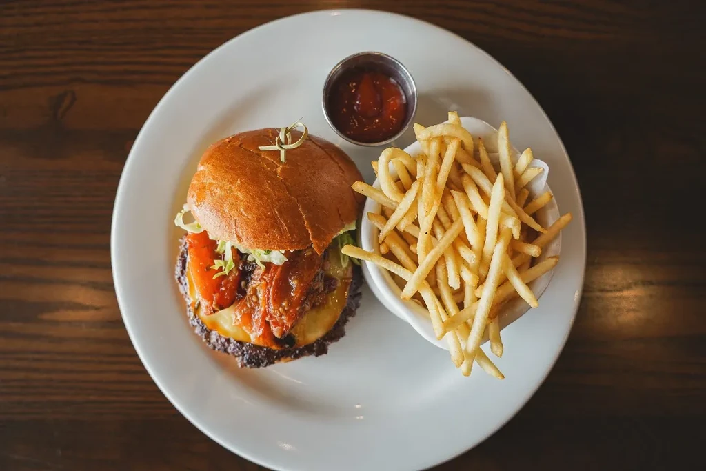 Plate with gourmet burger, fries, and ketchup on a wooden table.