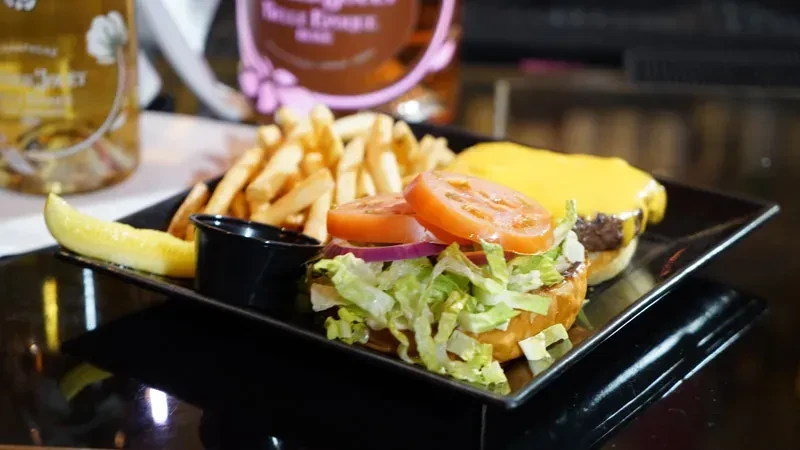 Burgers, fries, and pickle spear on a black rectangular plate.