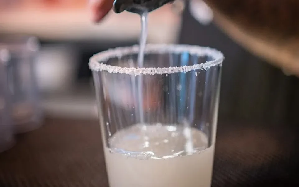A hand pours liquid into a clear glass with a salted rim.