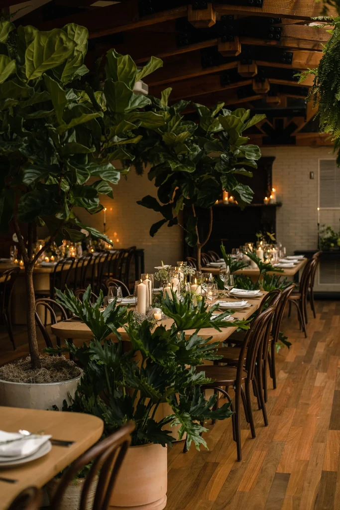 Elegant restaurant with long candlelit tables, plants, and wood details.
