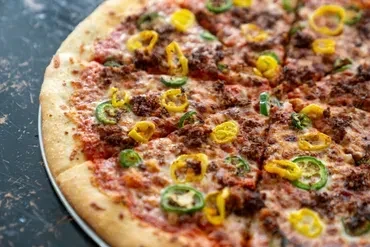 Sliced meat and cheese pizza topped with green and yellow peppers.