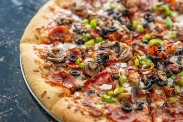 Freshly baked pizza with pepperoni, vegetables, sausage, and olives.