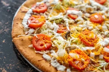 Close-up of pizza with tomato, lettuce, onion, white sauce, and orange strips.