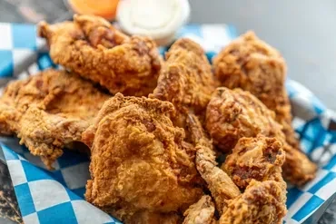 Golden-brown fried chicken in a checkered basket with dipping sauces.