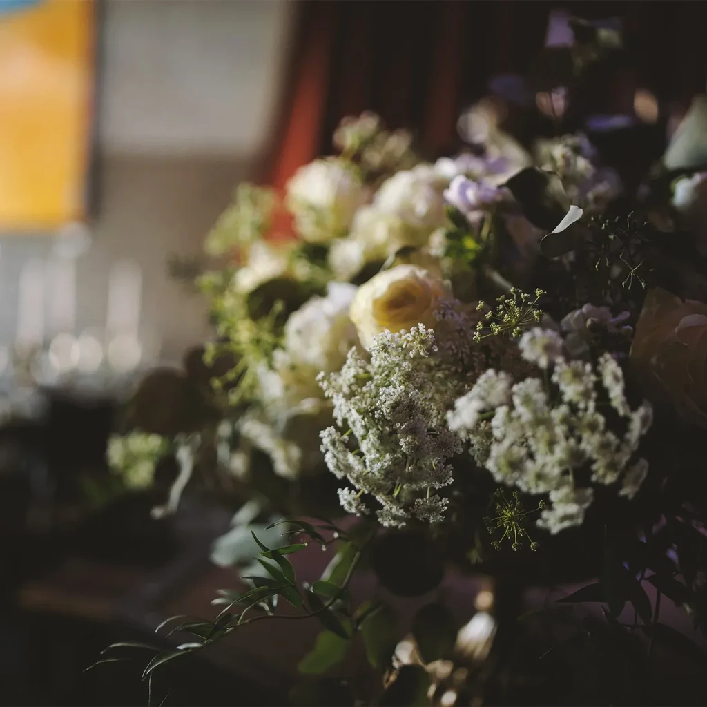Soft-focus floral arrangement with white and yellow roses in dim light.