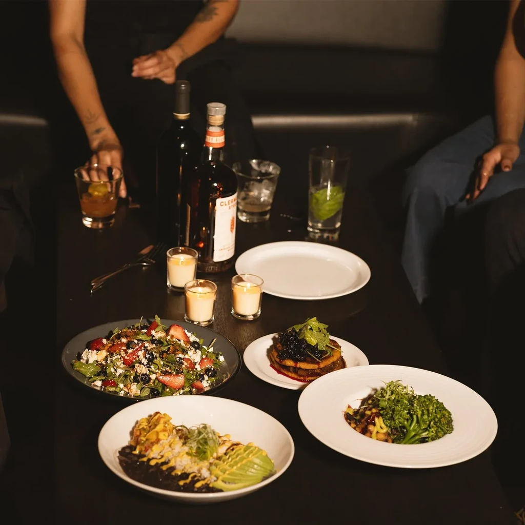 Dining table with diverse food, drinks, candles, and visible hands.