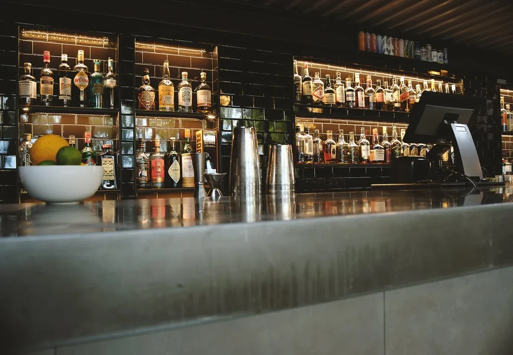 Modern bar interior with backlit liquor bottles, fruit, and bartender tools.