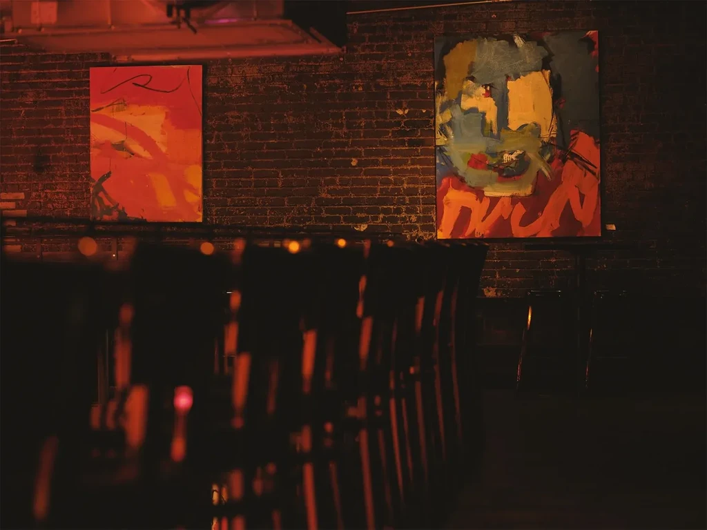 Two abstract paintings, one with "DUCK," on a dimly lit brick wall.