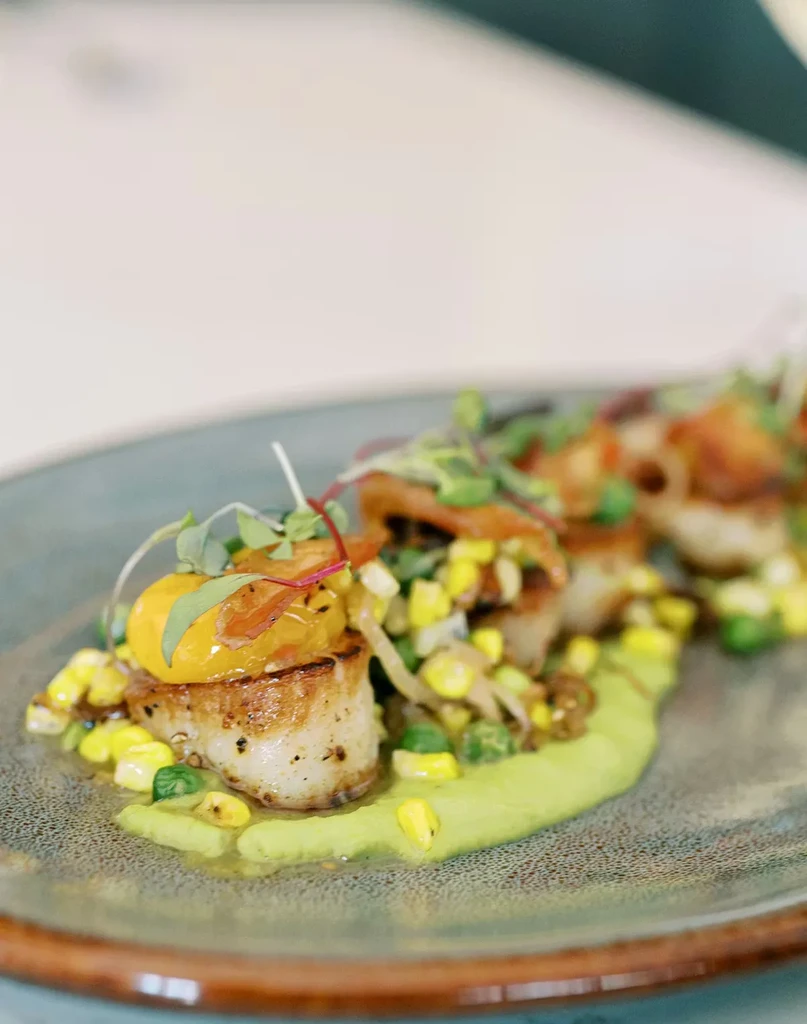 Elegantly plated seared scallops with tomato, microgreens, and green sauce.