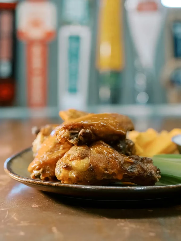 Plate of saucy chicken wings, celery, fries, and dip at a bar.