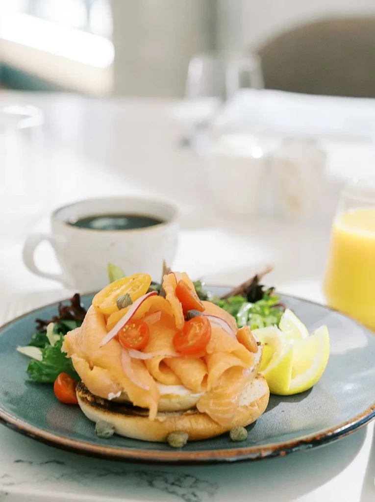 Close-up of a smoked salmon bagel, side salad, coffee, and orange juice.