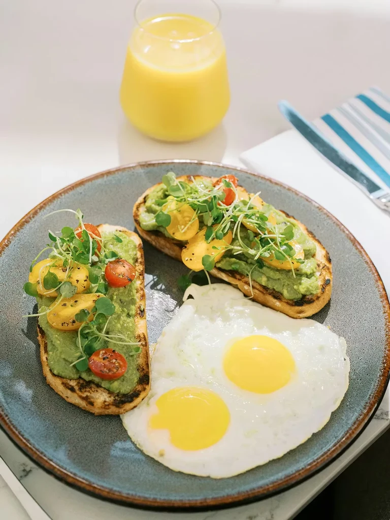 Two avocado toasts, fried eggs, tomatoes, microgreens, and orange juice.