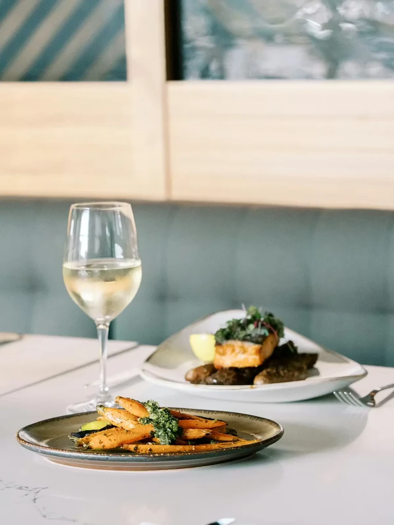 Roasted carrots with green sauce, white wine, and salmon in a restaurant.
