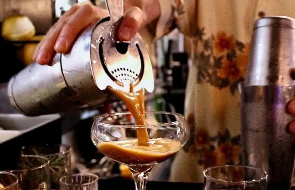 Bartender pours caramel drink from shaker into coupe glass.