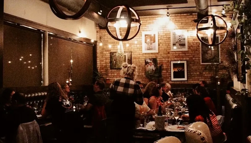 A bustling, rustic-chic restaurant interior with brick walls and diners.