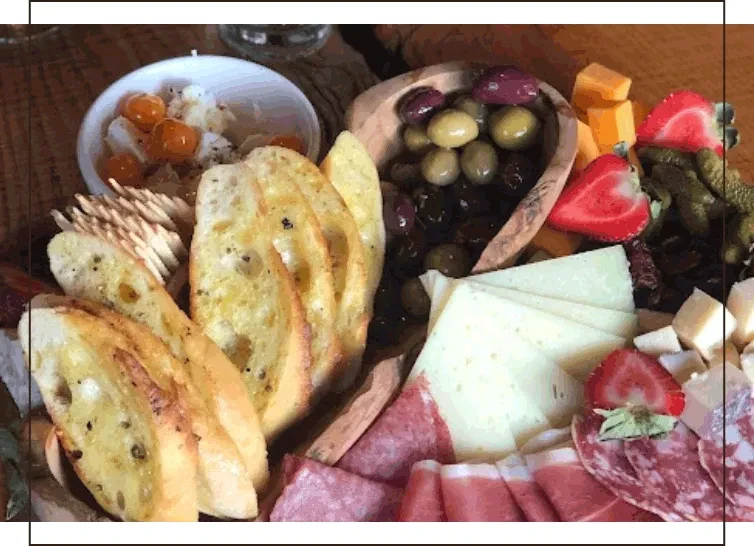 Rustic charcuterie board with cheeses, meats, bread, olives, and fresh fruit.