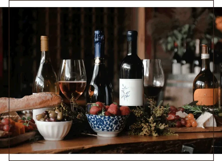 Wine bottles, cheeses, fruits, and snacks displayed on a wooden counter.