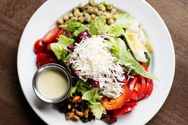Colorful salad with cheese, tomatoes, pesto chickpeas, artichokes, and dressing.