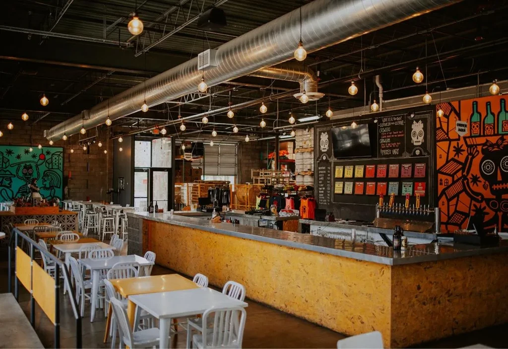 Spacious industrial-chic brewery interior featuring a bar and vibrant murals.