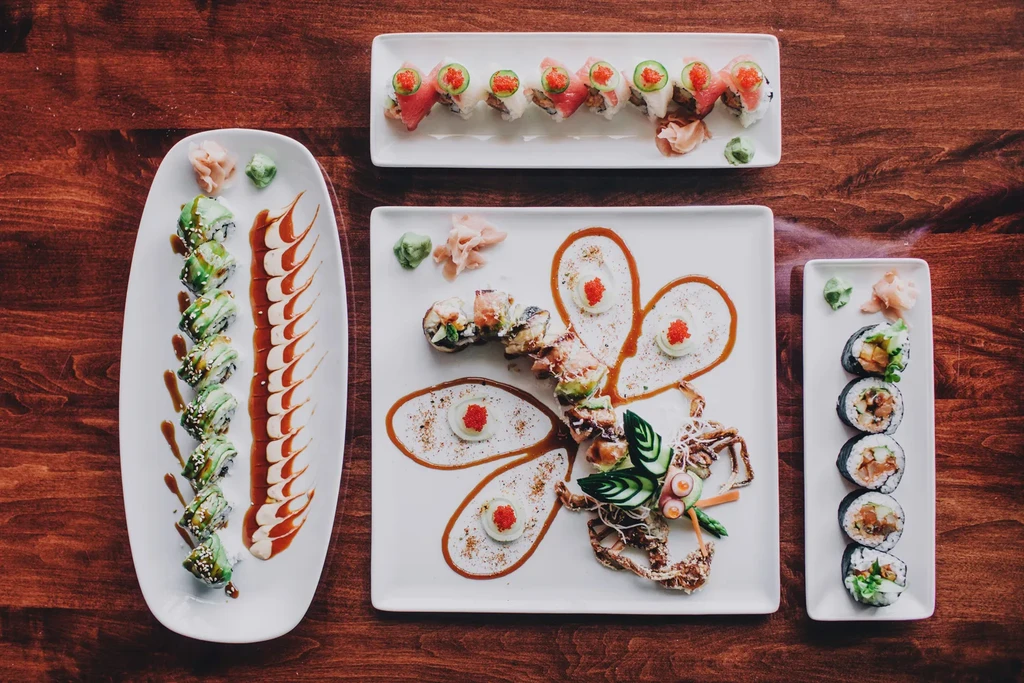Four plates of colorful, garnished sushi and Japanese food on wood.