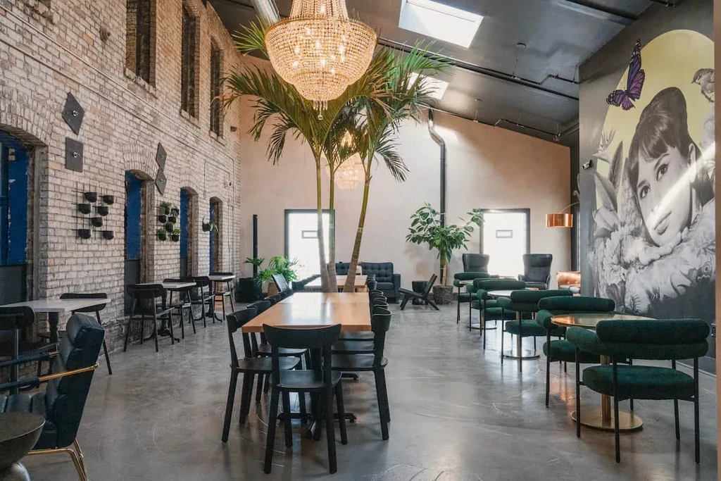 Stylish restaurant interior with brick, palm trees, and large mural.