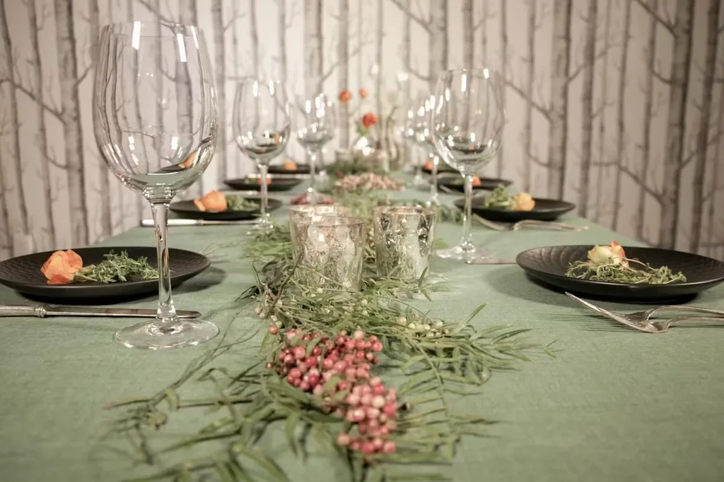 Elaborate dining table with natural green foliage, red berries, and dark plates.