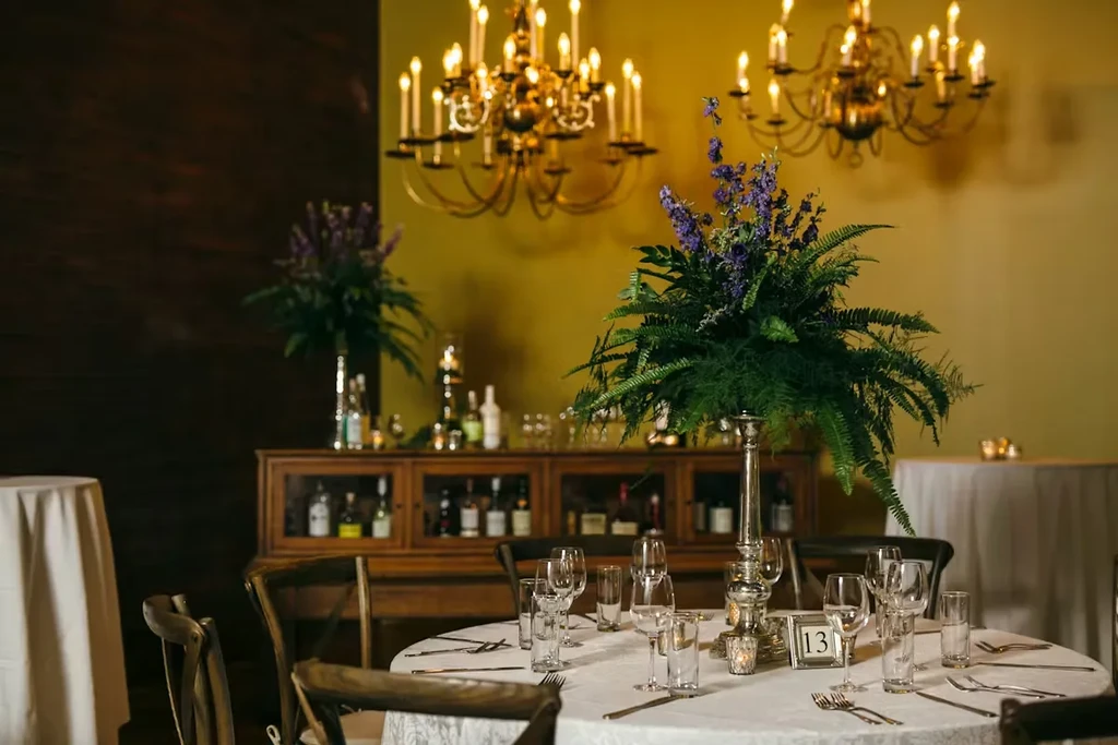 Elegantly set dining table with purple floral centerpiece and gold chandeliers.