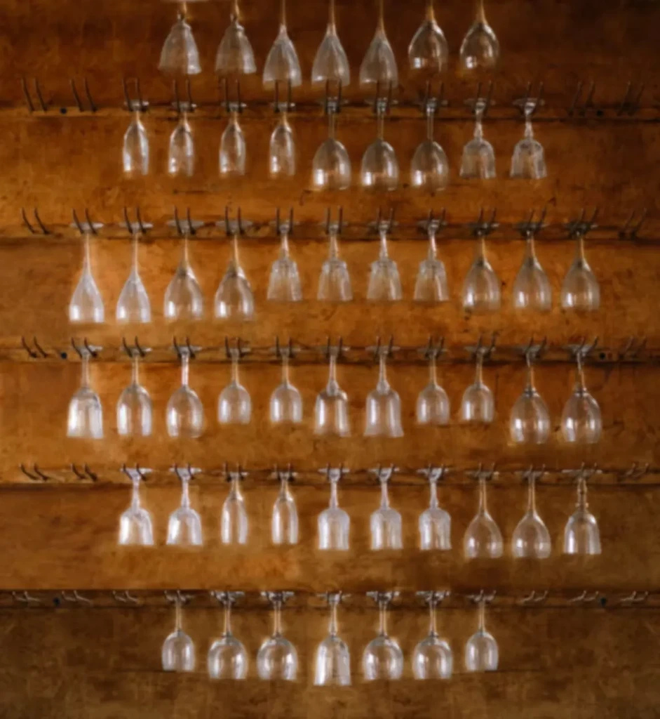 Clear glass goblets hang in symmetrical rows against a warm wooden wall.