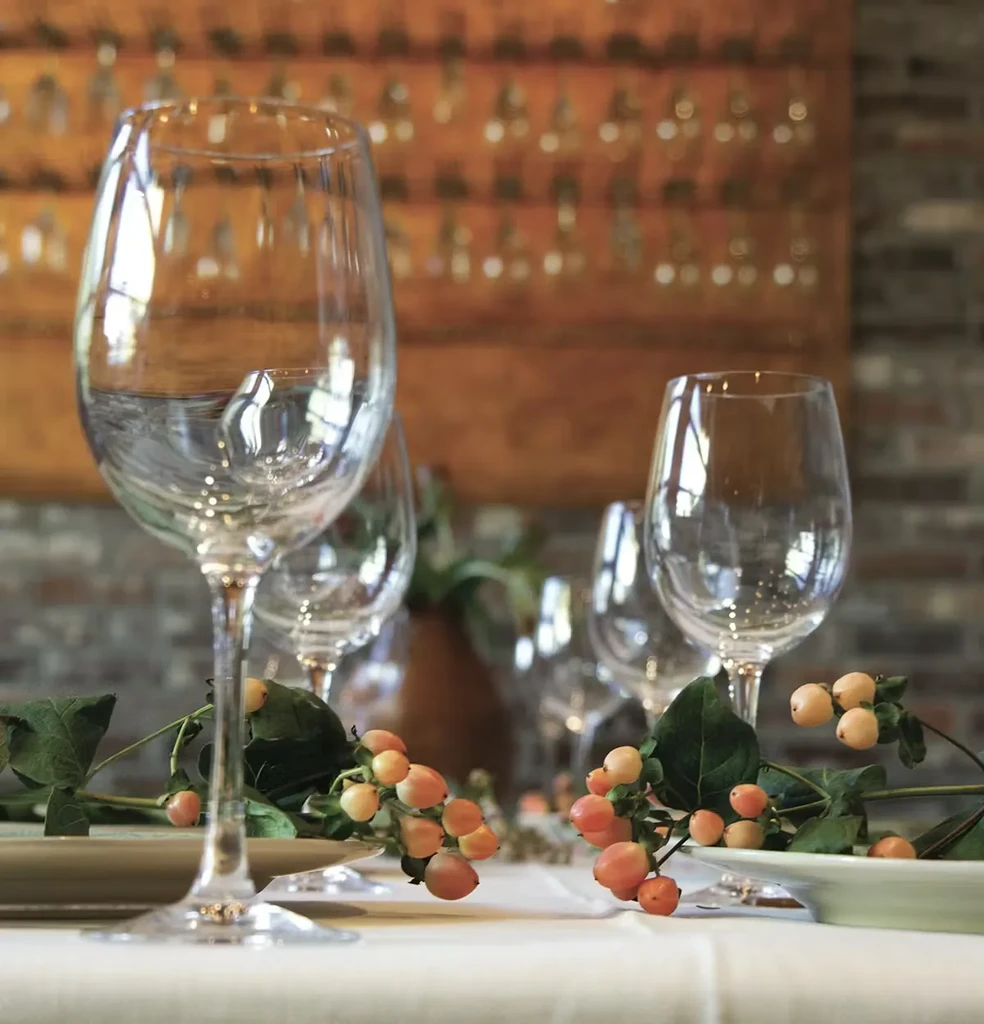 Set restaurant table with wine glasses, foliage, and orange berries.