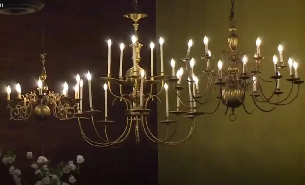 Two ornate brass chandeliers with candle-like bulbs illuminate a dim room.