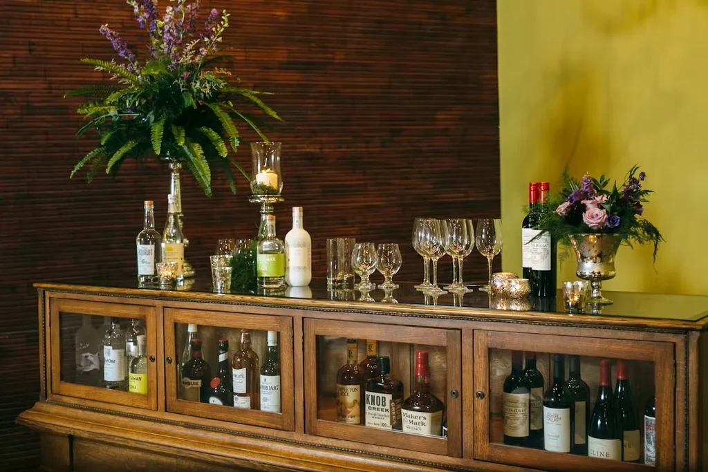 Elegant bar display with liquor, wine, empty glasses, purple flowers, and candles.