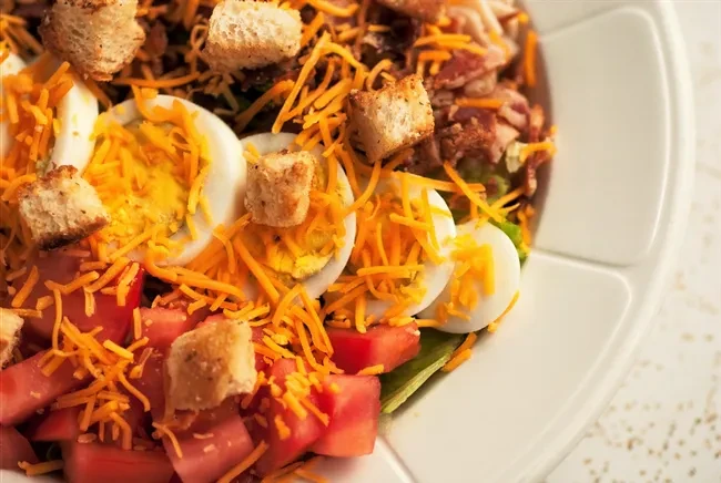 Colorful overhead salad with hard-boiled eggs, cheddar cheese, tomatoes, and croutons.