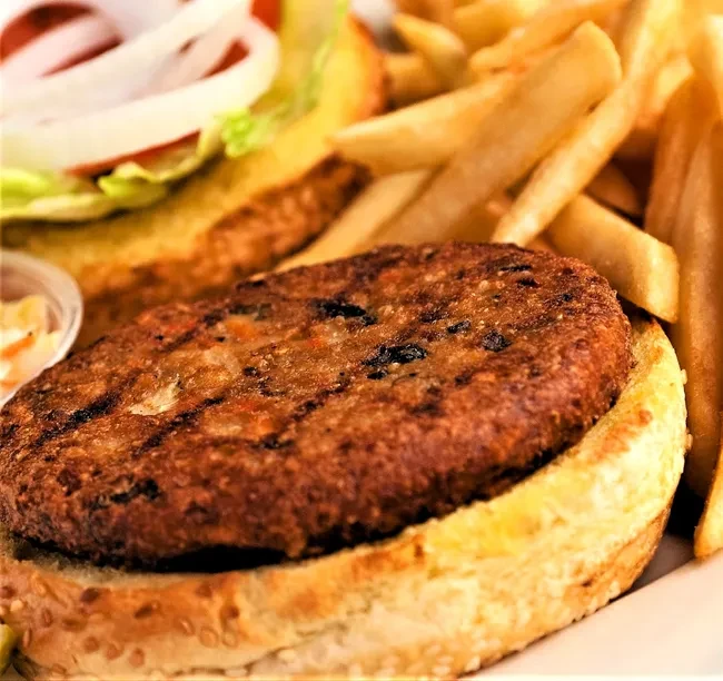 Grilled burger patty with grill marks, sesame bun, fries, lettuce, onion.