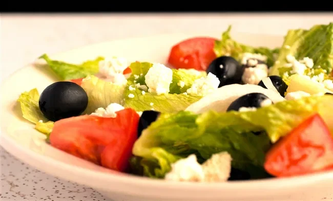 Close-up of fresh salad with lettuce, tomato, olives, and feta.