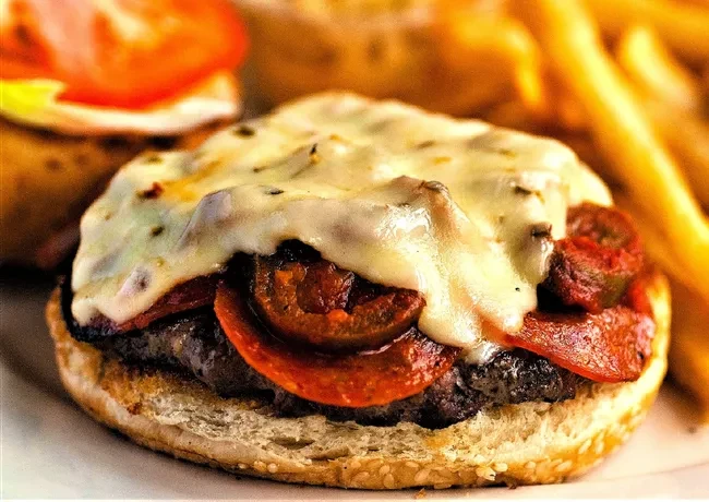 Beef burger with pepperoni, jalapeños, melted cheese on a sesame bun.