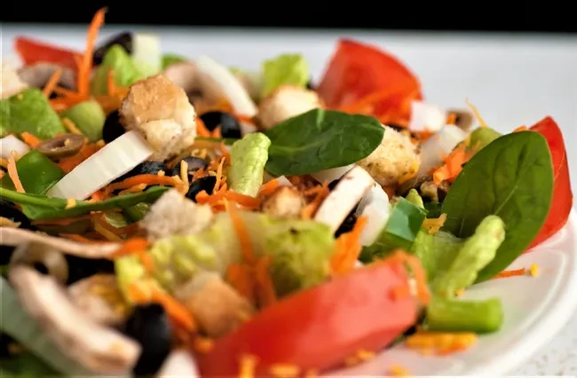 Close-up of fresh mixed salad with lettuce, tomatoes, carrots, olives.