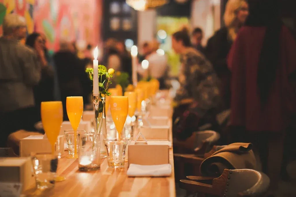 Candlelit table setting with drinks, flowers, and blurred people.
